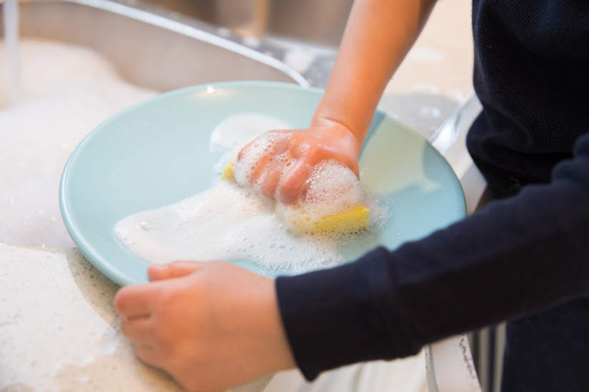 Close up of little boy's hands with sponge and soap suds washing a plate in the kitchen