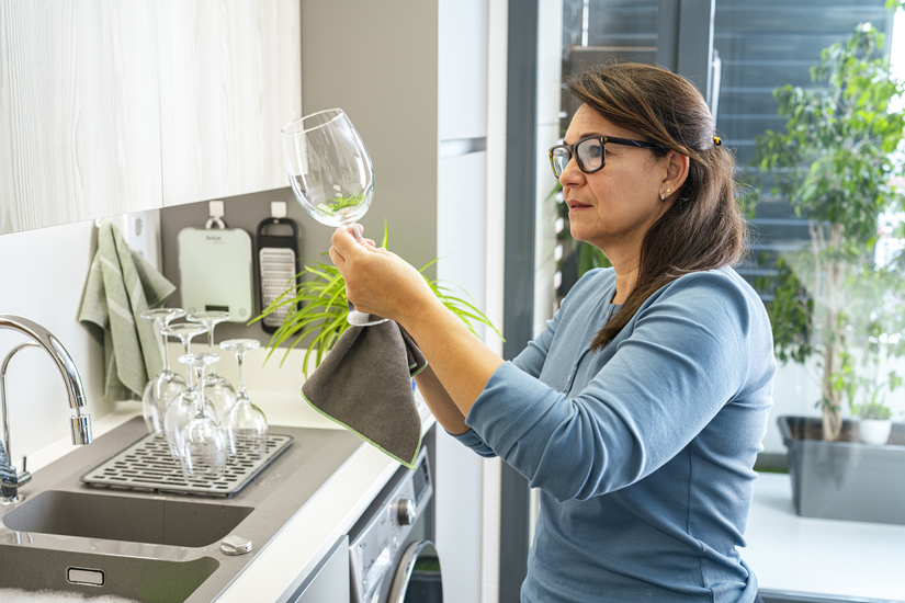 Woman examining a freshly washed wine glass for stains in the kitchen. High resolution 42Mp indoors digital capture taken with SONY A7rII and Zeiss Batis 40mm F2.0 CF lens