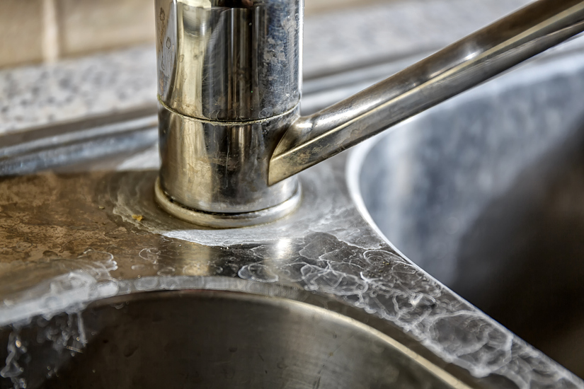 Close-up of a kitchen tap and sink with hard water calcification.