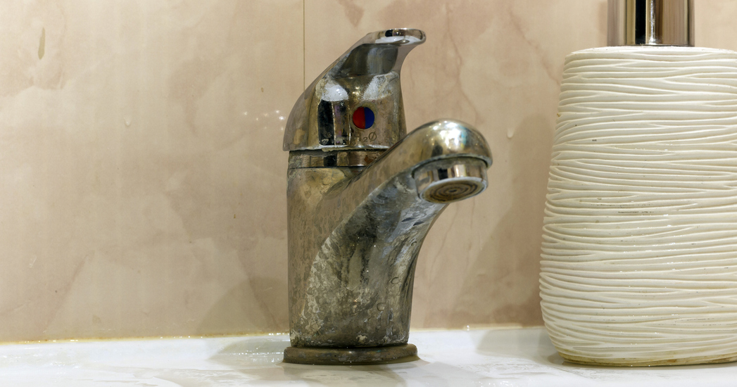 Old bathroom faucet with heavy lime scale buildup, showing signs of wear and neglect.